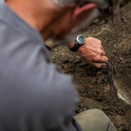 Archeoloog gebruikt een troffel om vondsten zichtbaar te maken in de bodem.