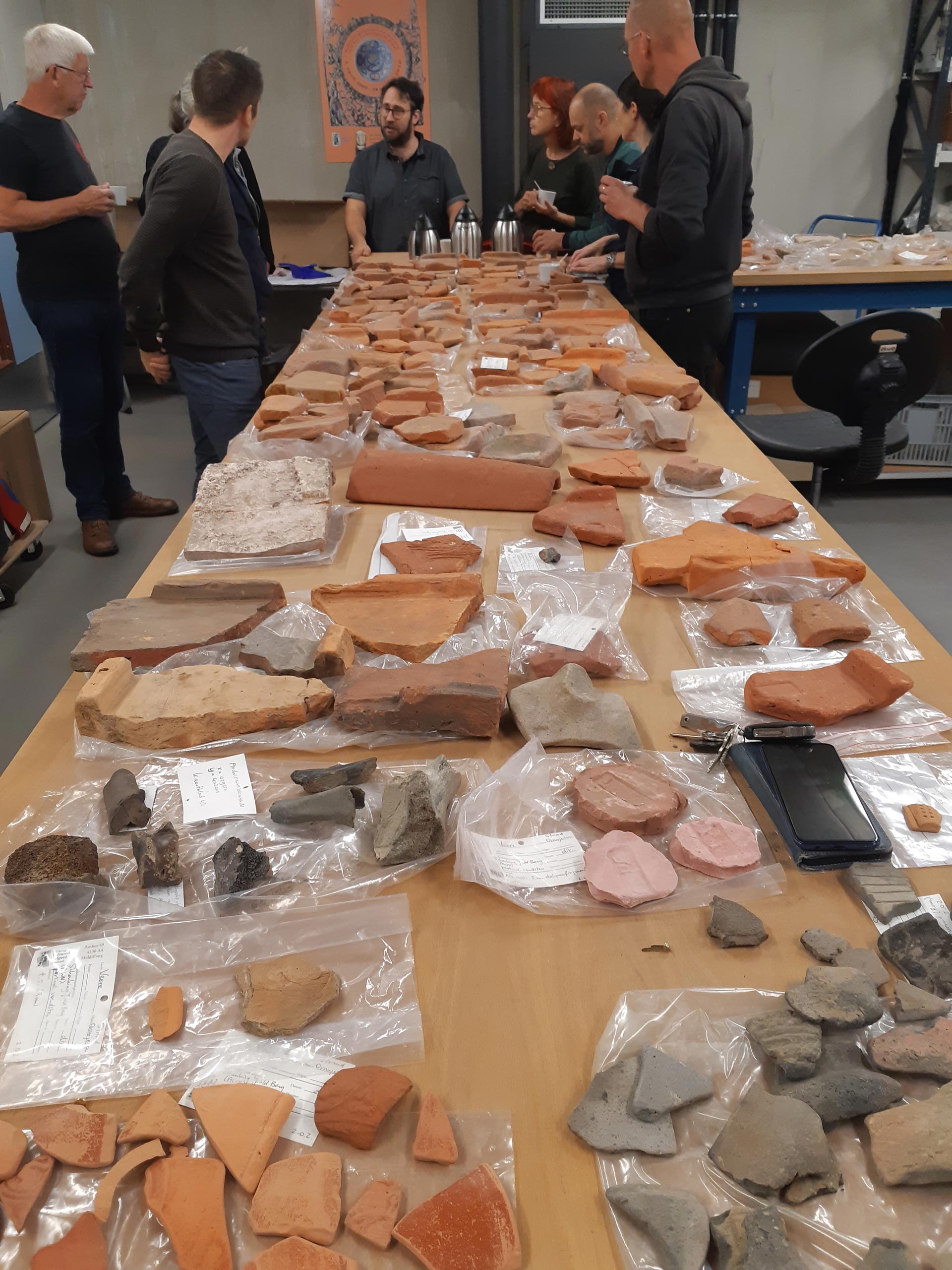 Strandvondsten van het project Beach Archaeology in de uitlegruimte van het depot, met onderzoekers eromheen.