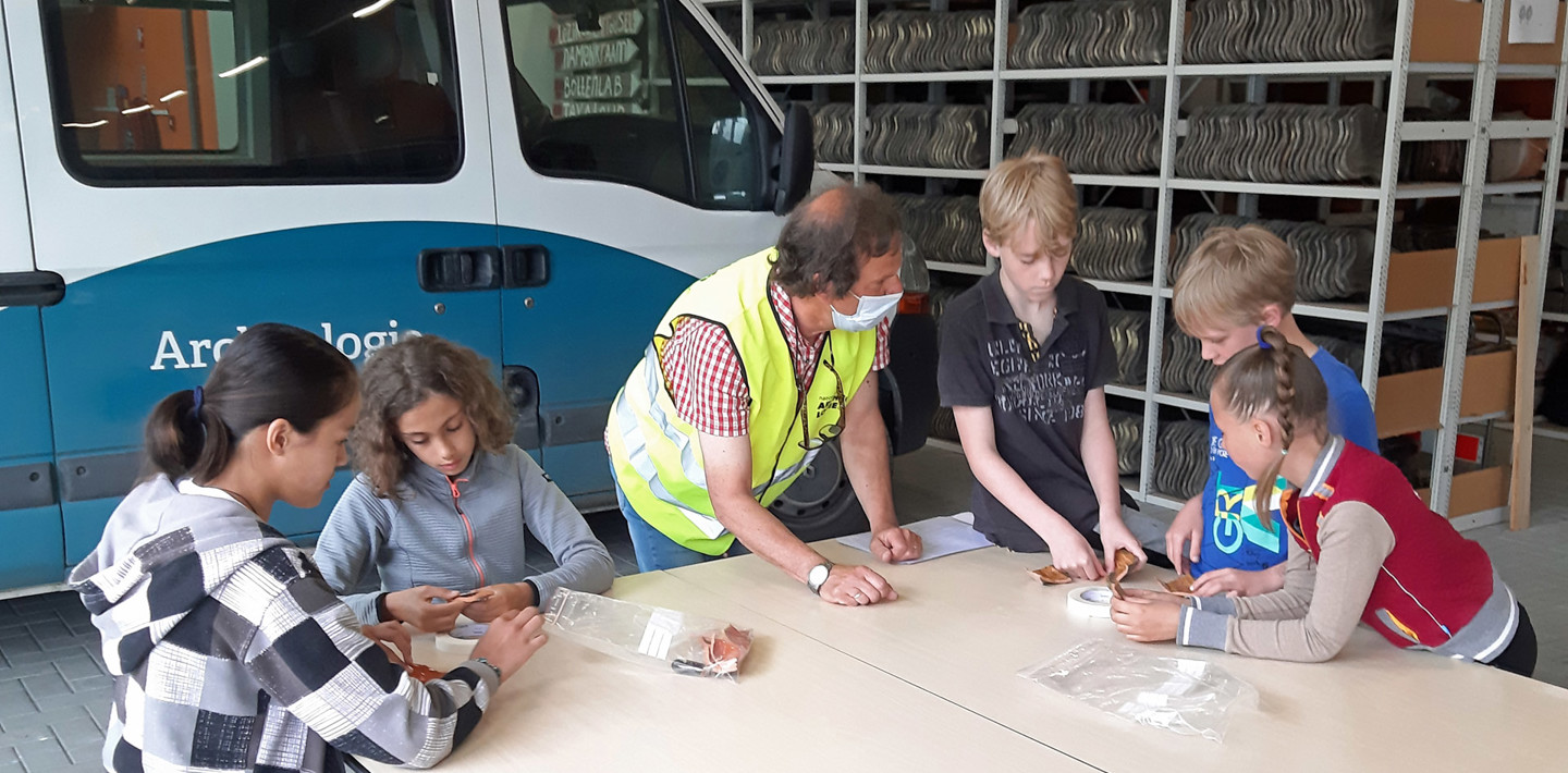 Kinderen puzzelen losse bakstenen scherven tot voorwerpen tijdens een kindercollege archeologie.