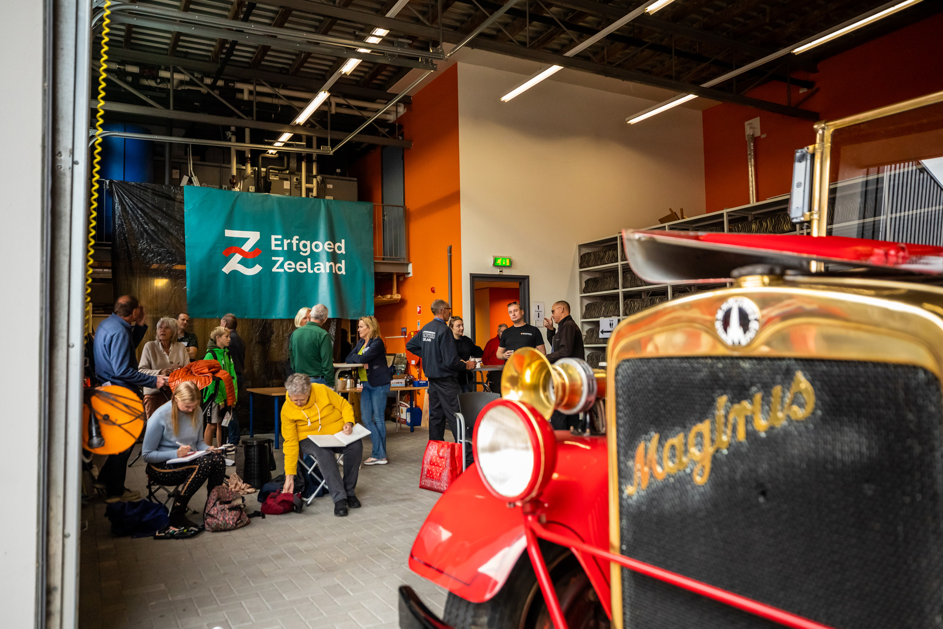 Mensen drinken koffie in de stallingsruimte met de Magirus op de voorgrond.