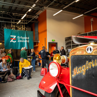 Mensen drinken koffie in de stallingsruimte met de Magirus op de voorgrond.
