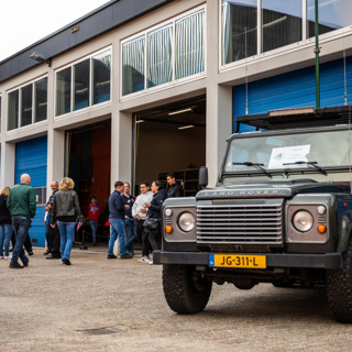 Landrover geparkeerd op het terrein voor de stallingsruimte met op de achtergrond lopende mensen.