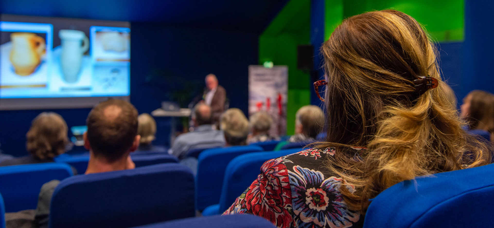 Deelneemster in zaal met op de achtergrond een PowerPoint-presentatie. 