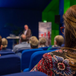 Deelneemster in zaal met op de achtergrond een PowerPoint-presentatie. 