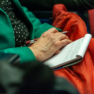 Close-up van een notitieboekje op de schoot van iemand die een pen vasthoudt. 
