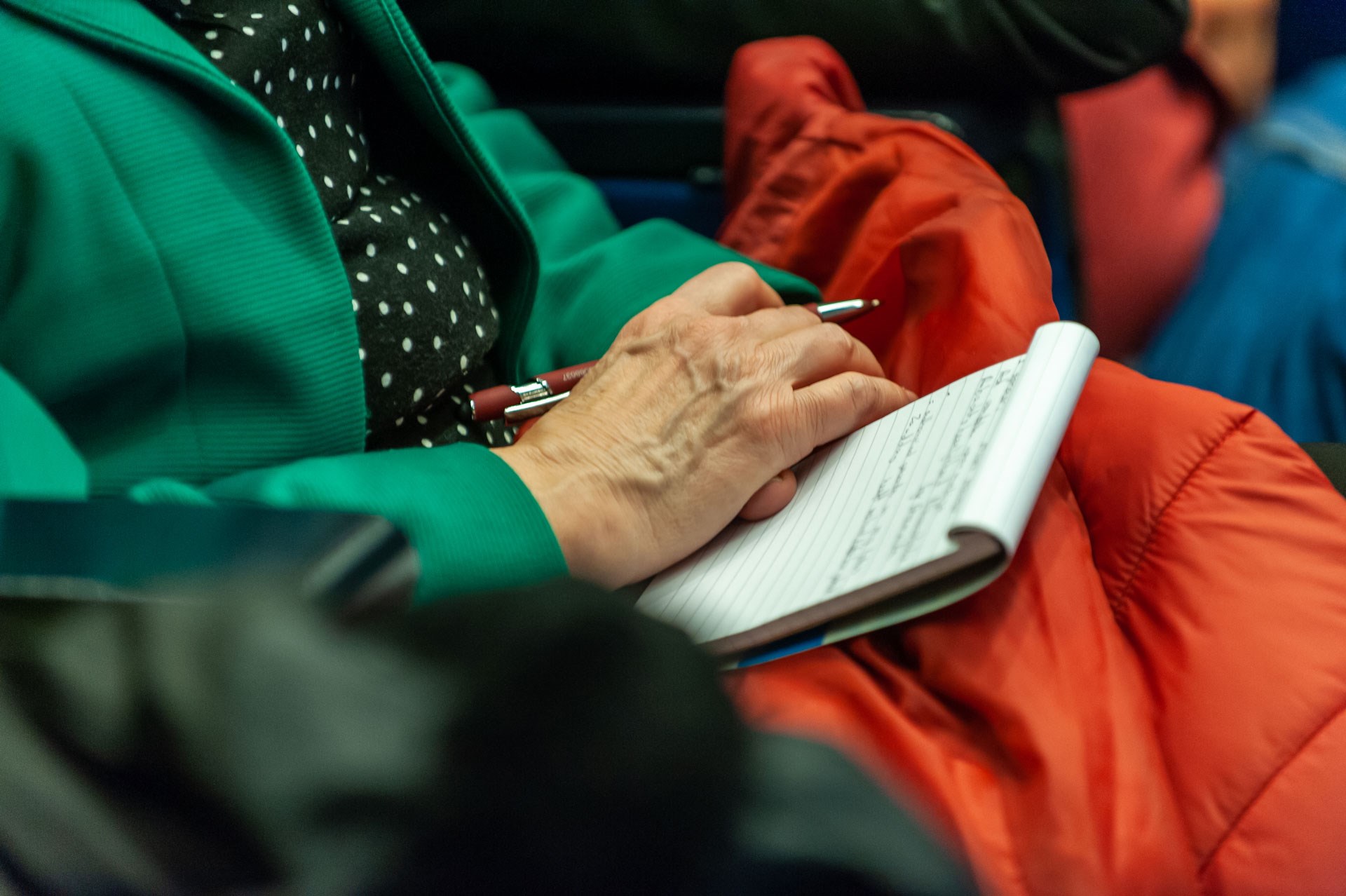 Close-up van een notitieboekje op de schoot van iemand die een pen vasthoudt. 