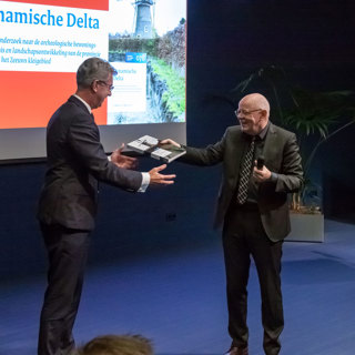 Leonard de Wit van de Rijksdienst voor het Cultureel Erfgoed overhandigt de onderzoekssynthese aan gedeputeerde Harry van der Maas. Foto Niek Beeke.