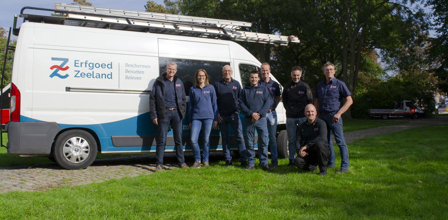 Het team Monumentenwacht, buiten poserend voor een monumentenwachtbus