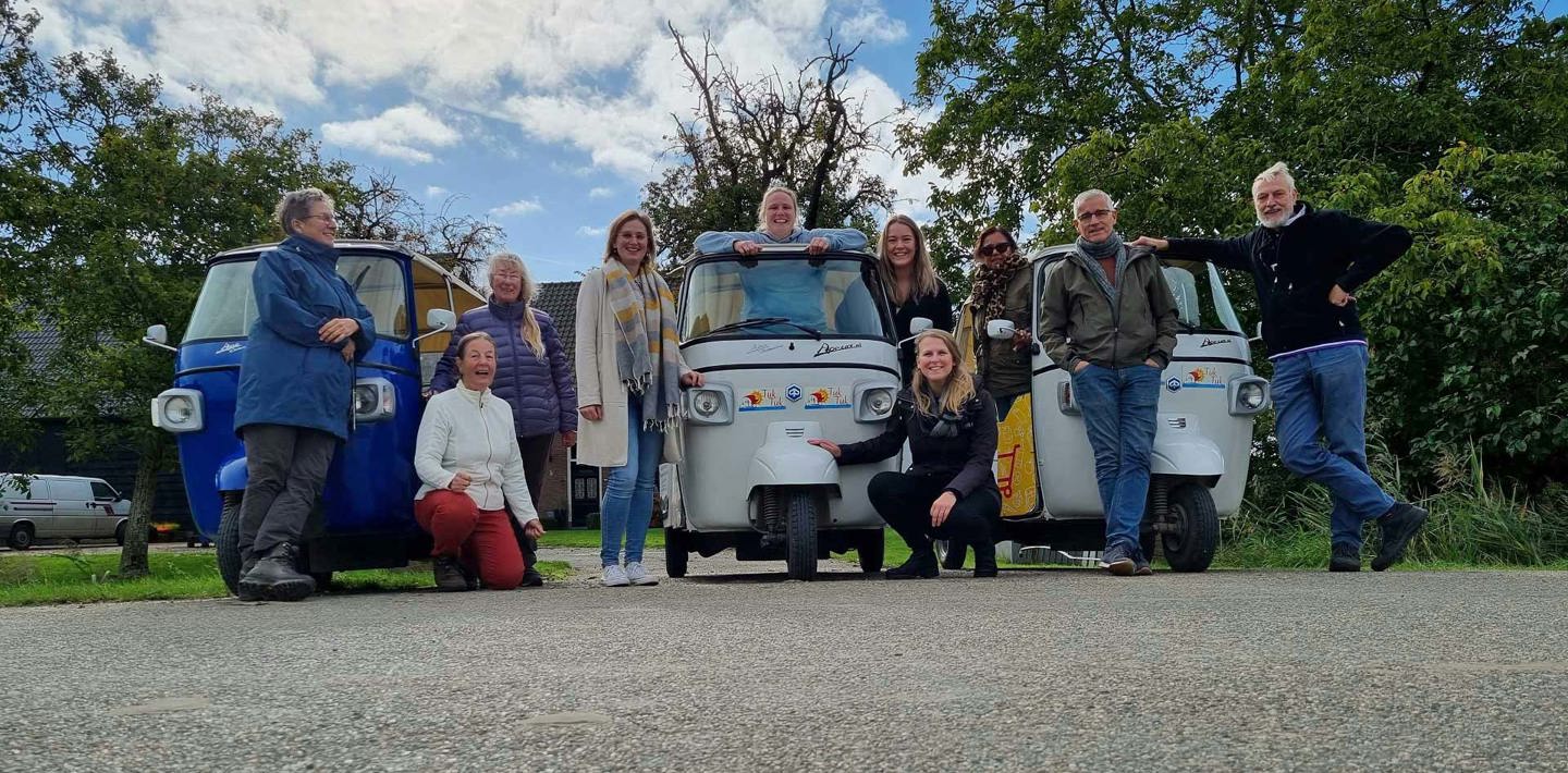 Groepjes medewerkers en vrijwilligers poseren voor TukTuk-wagentjes tijdens een personeelsuitje.
