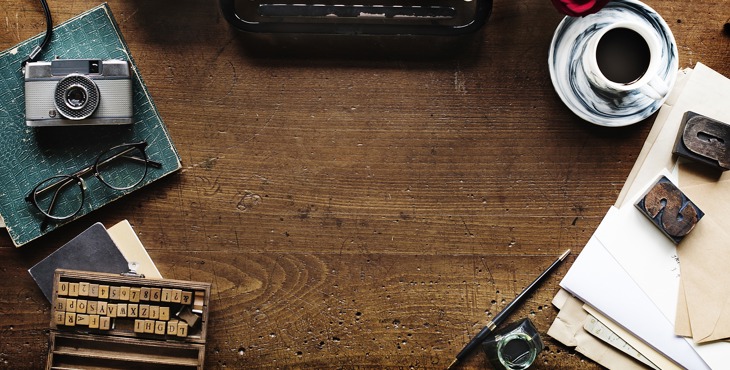 Een bureau van bovenaf met oude typemachine, fototoestel, stempels en een kopje koffie.