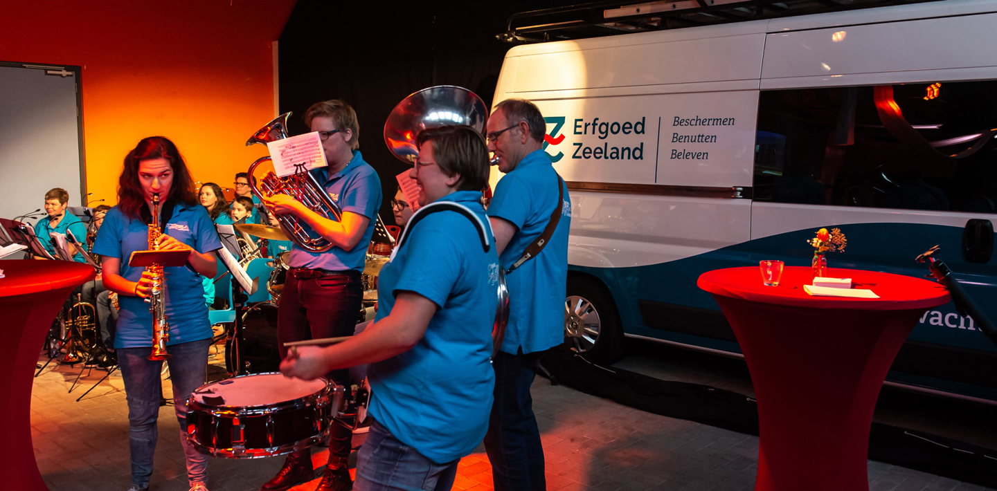 Het Julianakorps speelt naast een bus van de Monumentenwacht van Erfgoed Zeeland.