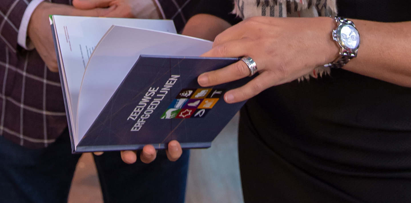 Vrouw houdt het boekje Zeeuwse Erfgoedlijnen vast tijdens de publicatie.