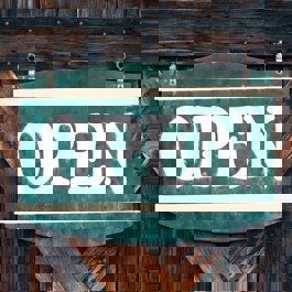 Aan een houten deur hangt een groen bordje met de tekst 