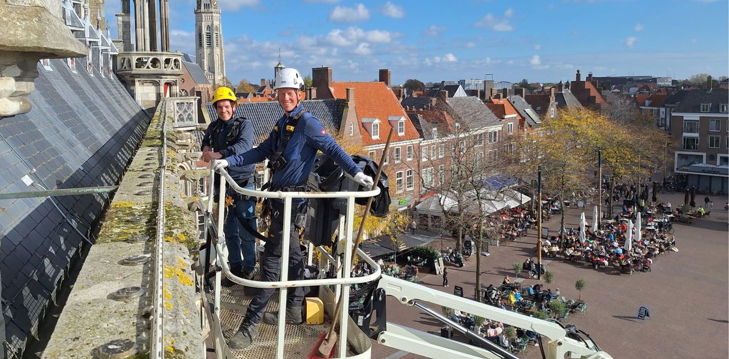 Monumentenwachters Sem de Paauw en Leon Leendertse inspecteren in een hoogwerker het oude stadhuis van Middelburg.
