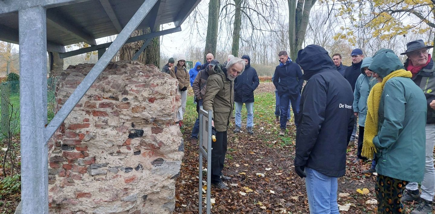 Een groep mensen krijgt buiten uitleg bij een restant van een historische muur in het Geopark Schelde Delta.