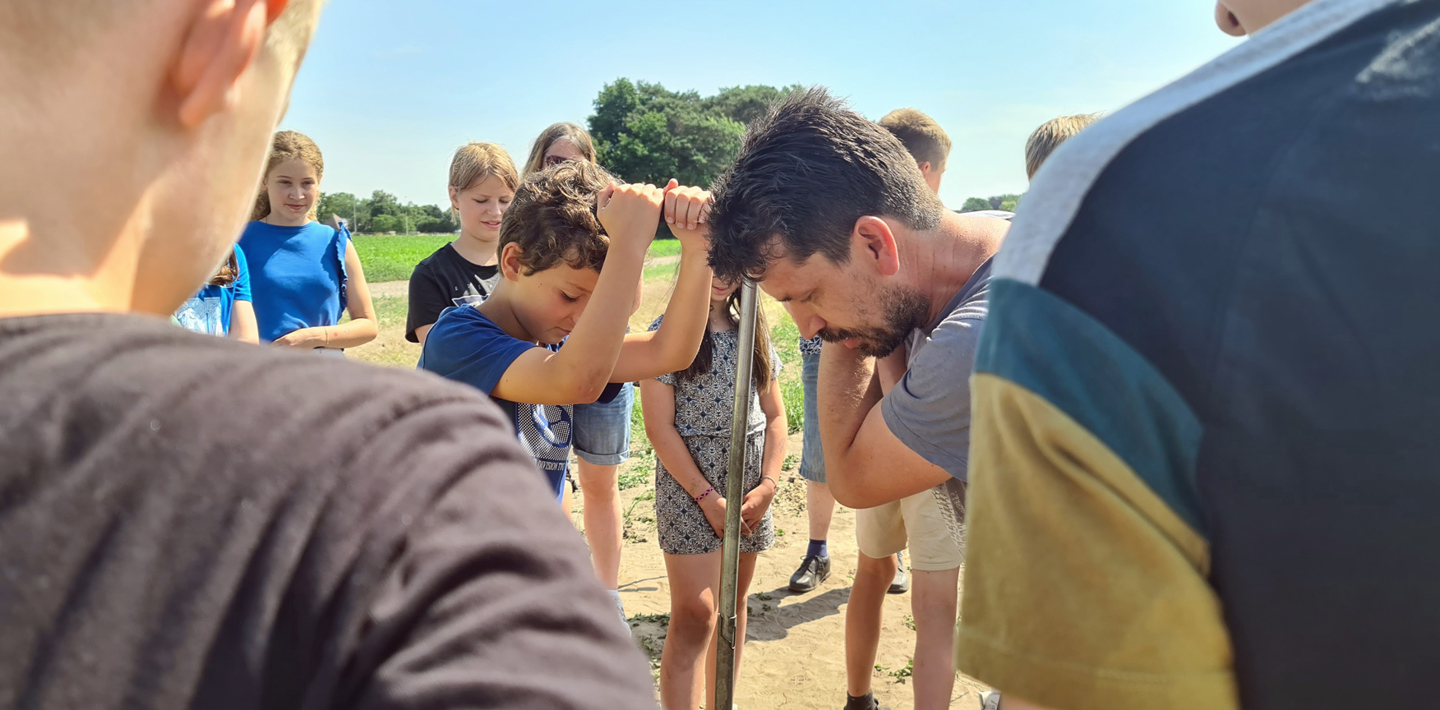 Leerlingen krijgen uitleg van een archeoloog over een grondboor tijdens de gastles 