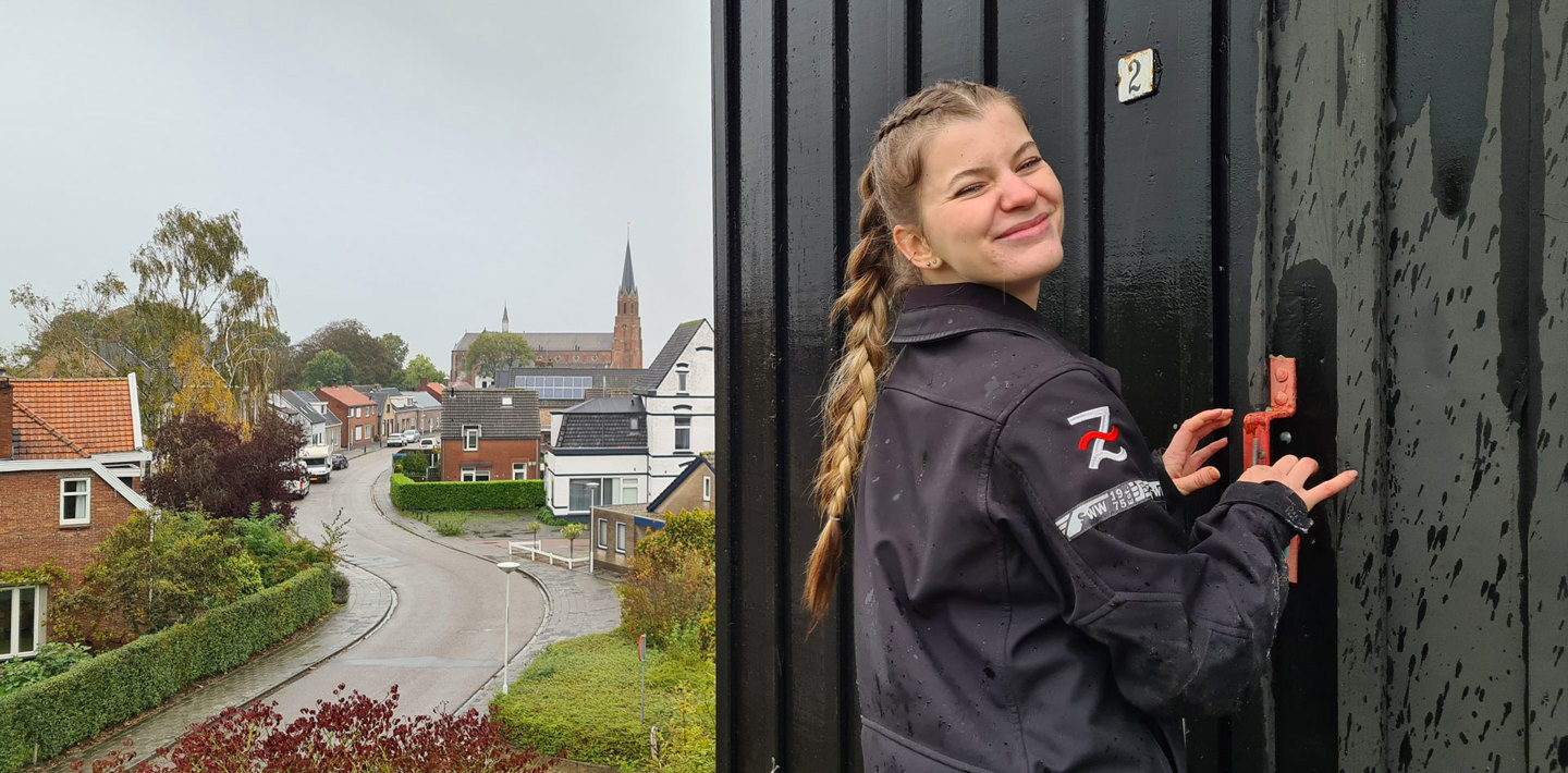 Een studente Bouwkunde sluit symbolisch haar afstudeerstage bij de Monumentenwacht af voor de deur van een molen.