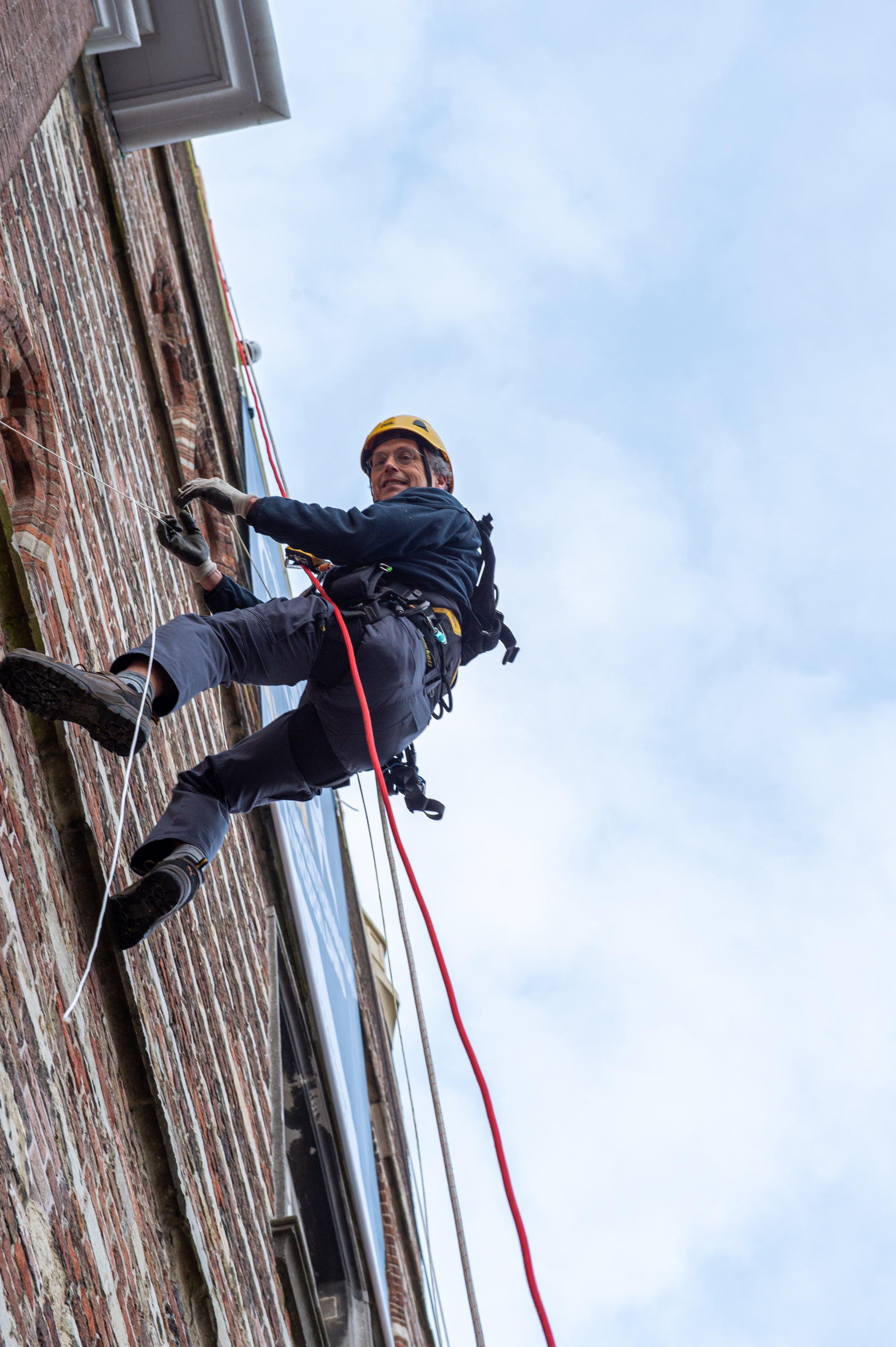 Monumentenwachter Coert van Spall rolt abseilend aan de gevel van het oude stadhuis aan de Grote Markt de banner uit.