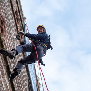 Monumentenwachter Coert van Spall rolt abseilend aan de gevel van het oude stadhuis aan de Grote Markt de banner uit.