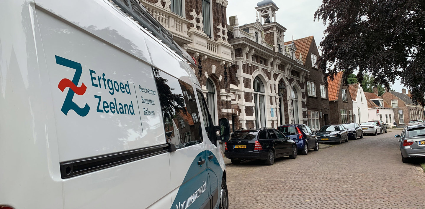 De bus van de Monumentenwacht van Erfgoed Zeeland in een straat met monumentale panden in Kloetinge.