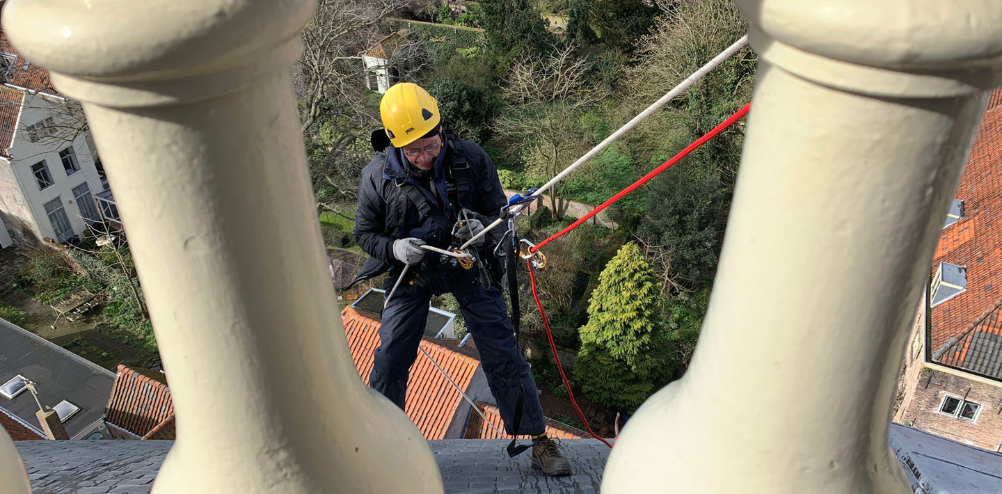 Een monumentenwachter in veiligheidsuitrusting inspecteert op grote hoogte de Oostkerk in Middelburg.
