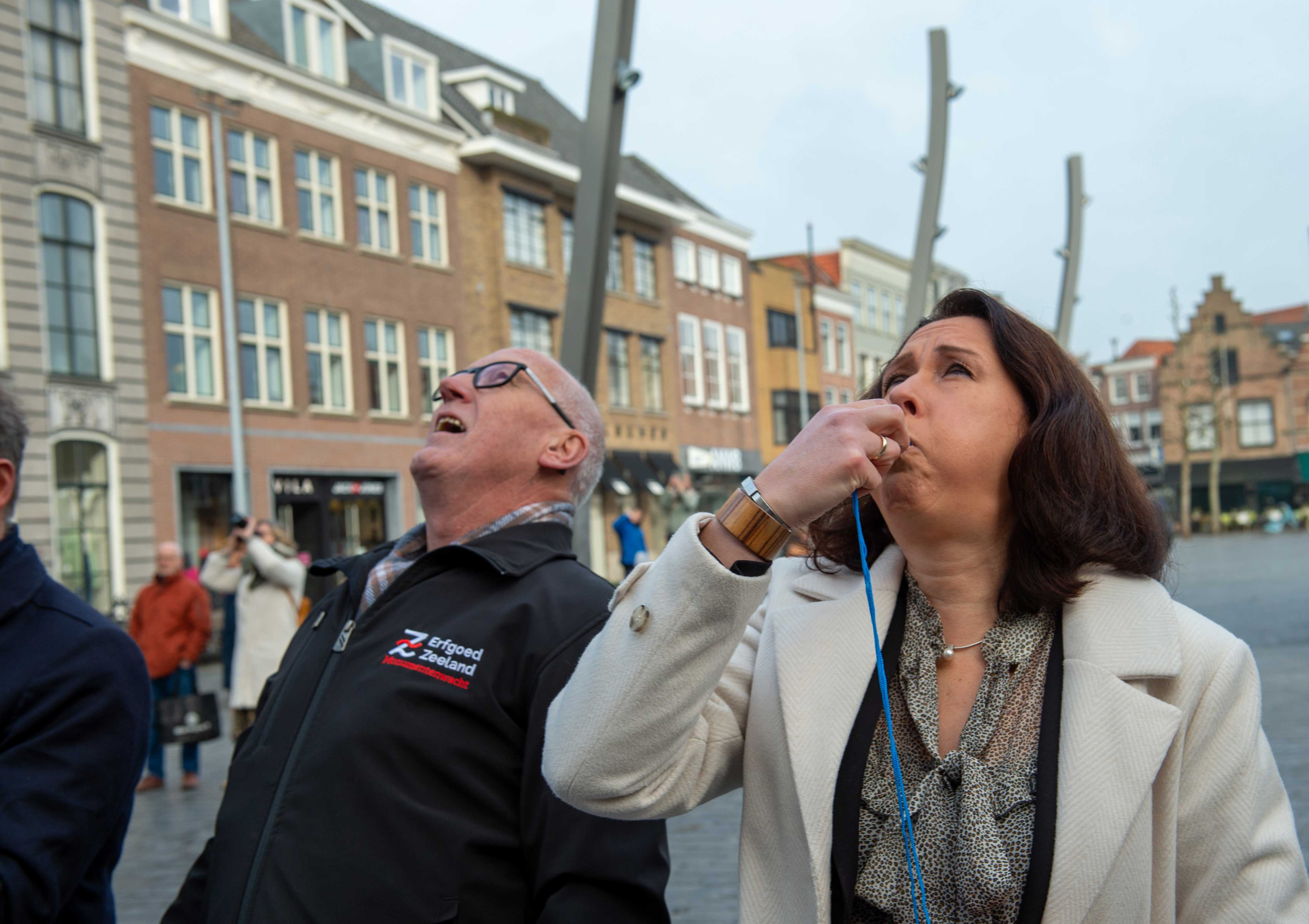Cultuurgedeputeerde Anita Pijpelink geeft op een fluitje het startsein voor het uitrollen van de banner, met naast haar teamleider Monumentenwacht Wim Jakobsen.