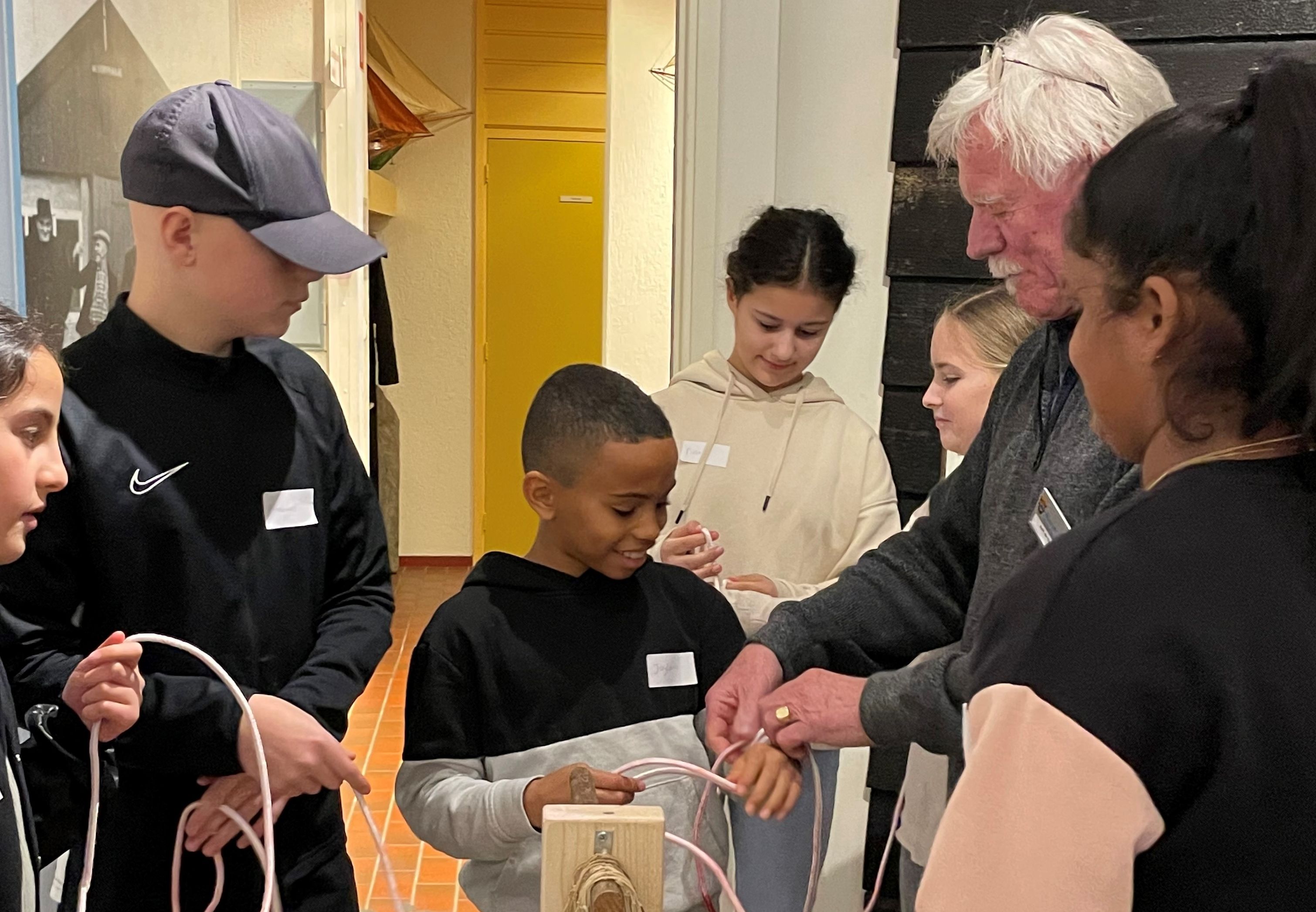 De rondleider van Museum Arnemuiden laat een groep kinderen zien hoe ze visnetten moeten knopen.