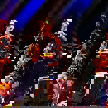 Een drietal mannen die op een podium muziek maken.
